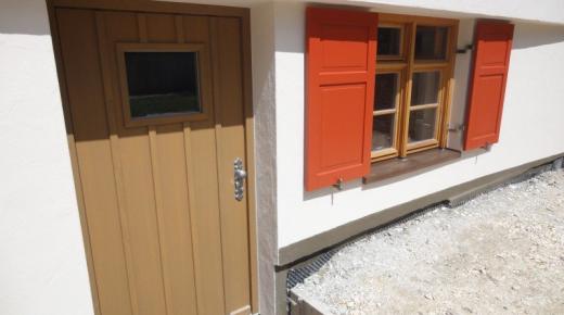 Sprossenfenster Holz mit orangenen Klappläden und Holz-Haustür